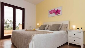 A bedroom with a bed, nightstands, a lamp, and a picture of pink flowers on the wall. - Finca Son Puca (Petra)