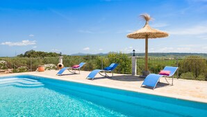 A swimming pool with clear blue water, surrounded by lounge chairs and a thatched umbrella. - Finca Son Puca (Petra)