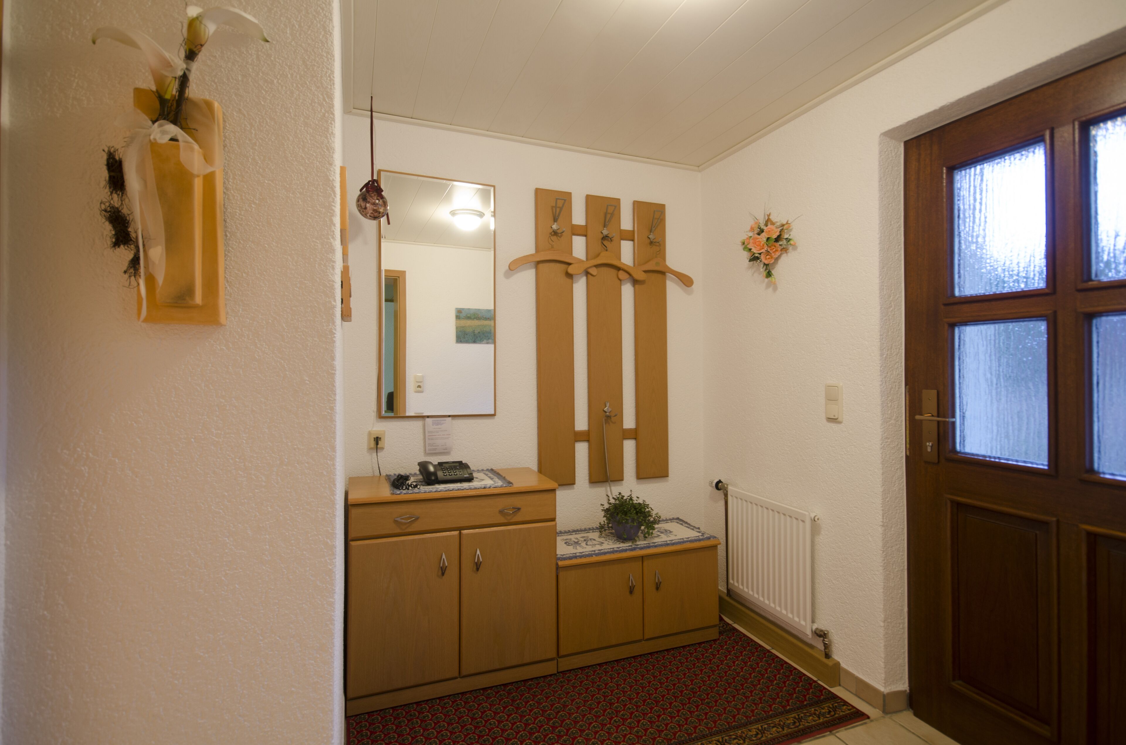 A hallway with a wooden cabinet, a mirror, a coat rack, and a door with frosted glass panels.