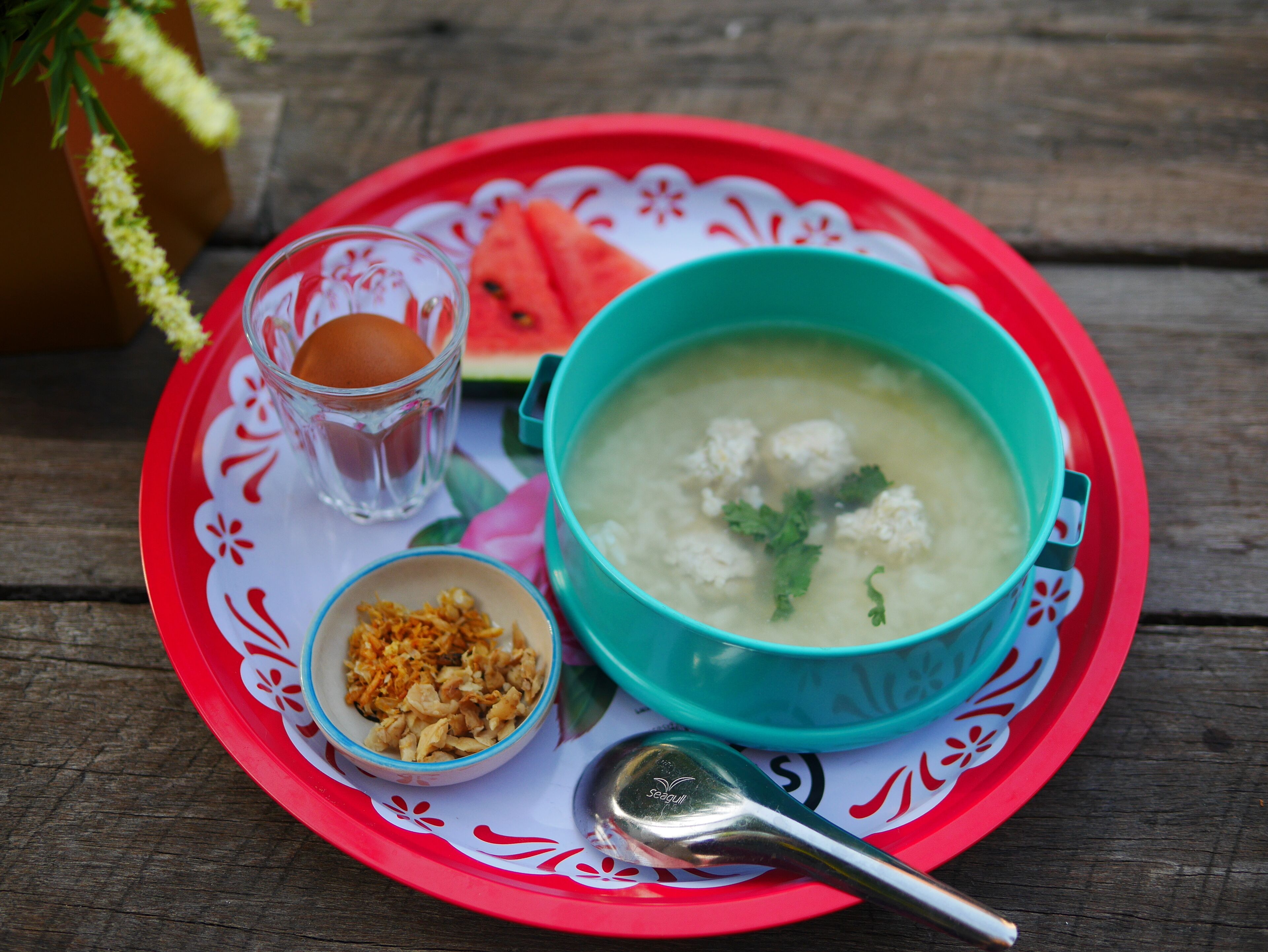 A meal with soup, a boiled egg, and a small bowl of fried shallots on a red tray.