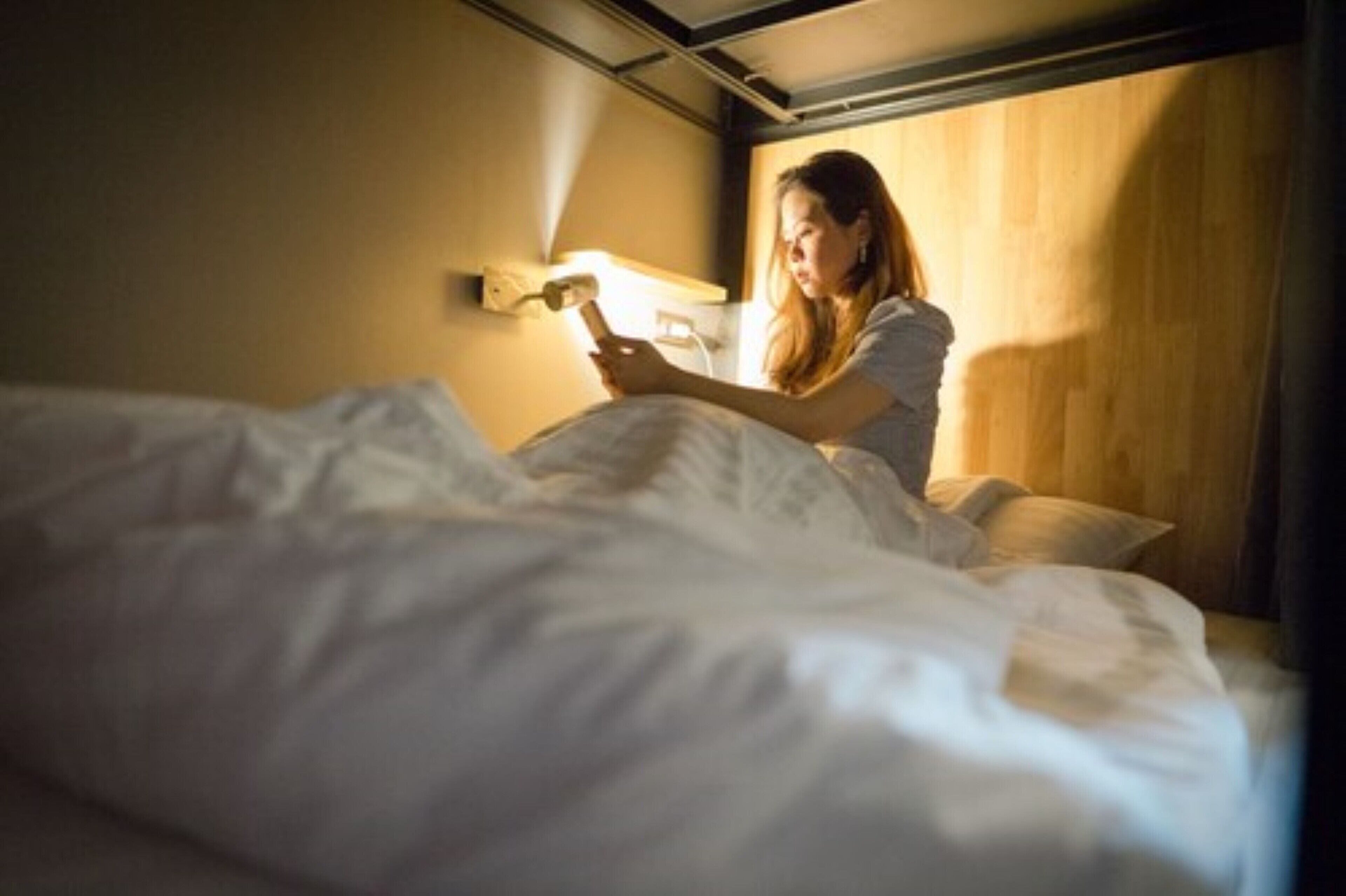 A person sitting on a bed in a room with a wooden headboard and a bedside lamp.