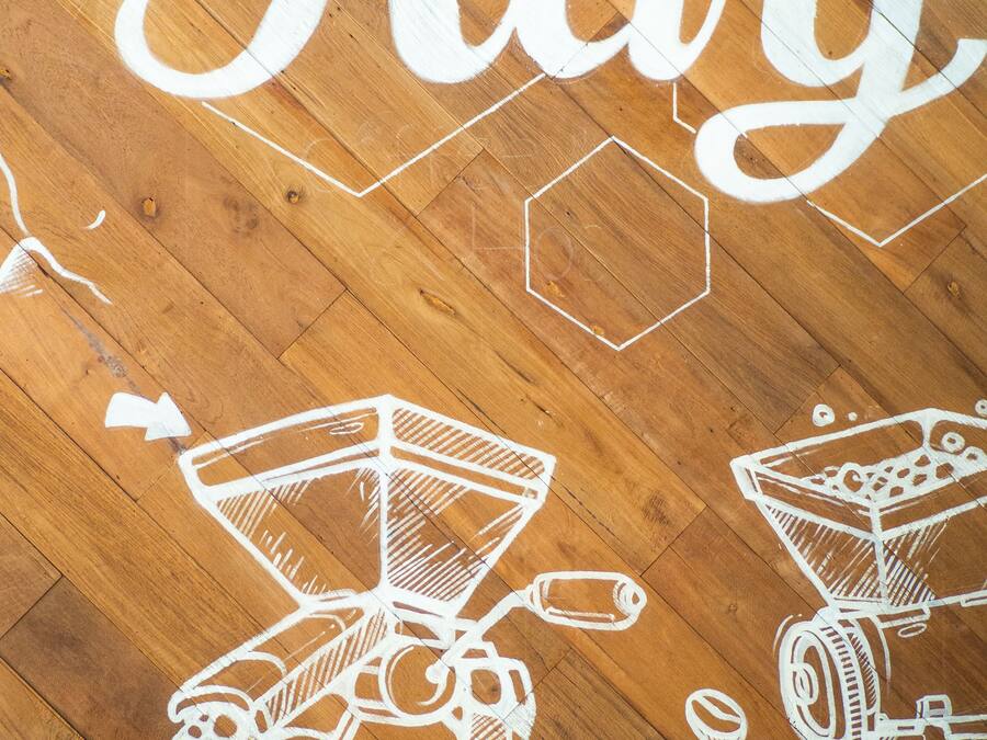 A wooden floor with white text and illustrations of coffee-making equipment.