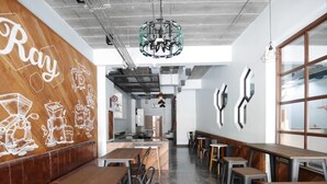 A modern cafe interior with wooden tables and chairs, a coffee machine, and a wall with coffee-related illustrations. - Ray Hostel (Chiang Mai)