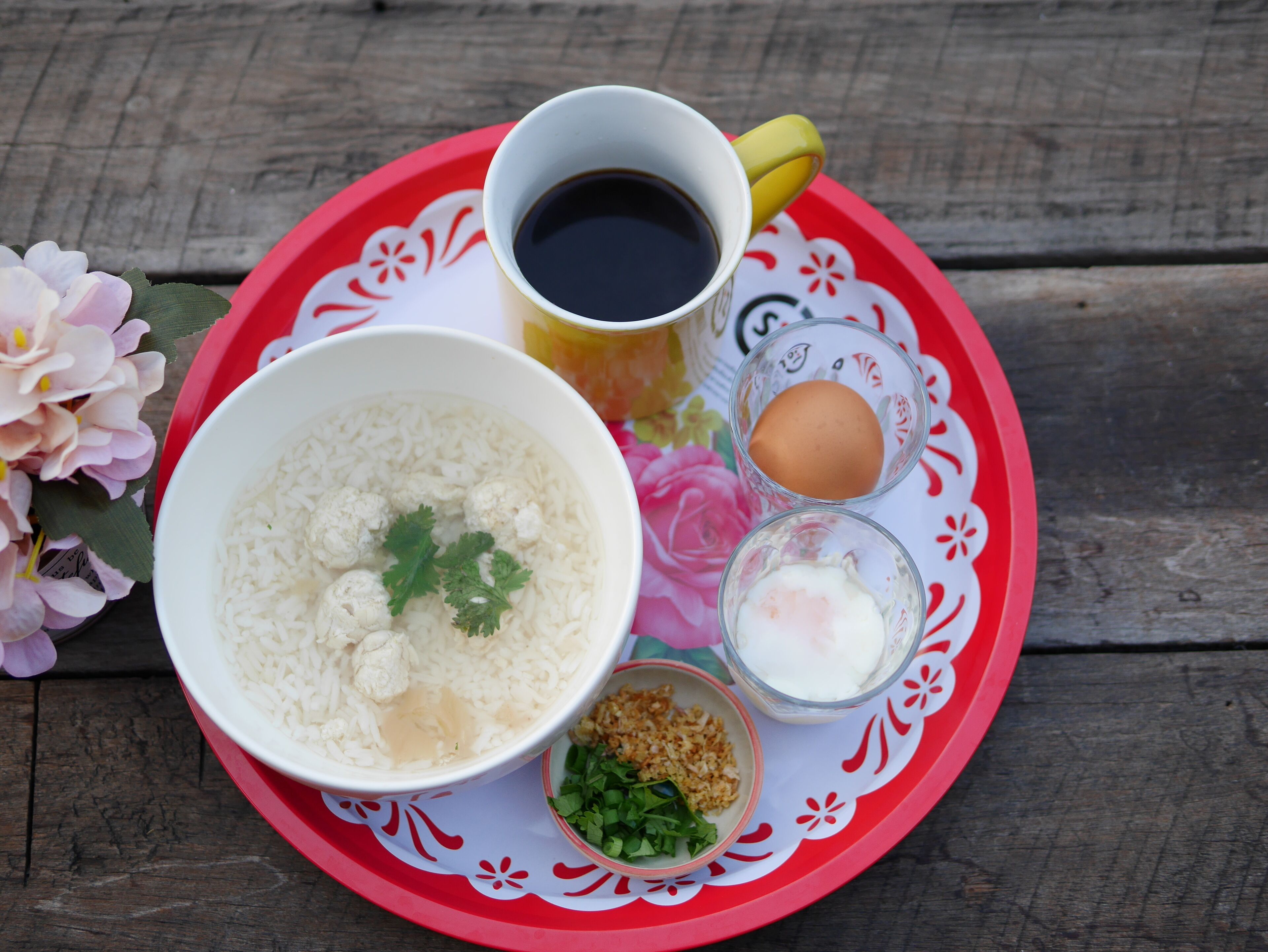 A tray with a bowl of rice, a cup of coffee, a glass of milk, a boiled egg, and a small bowl of greens.