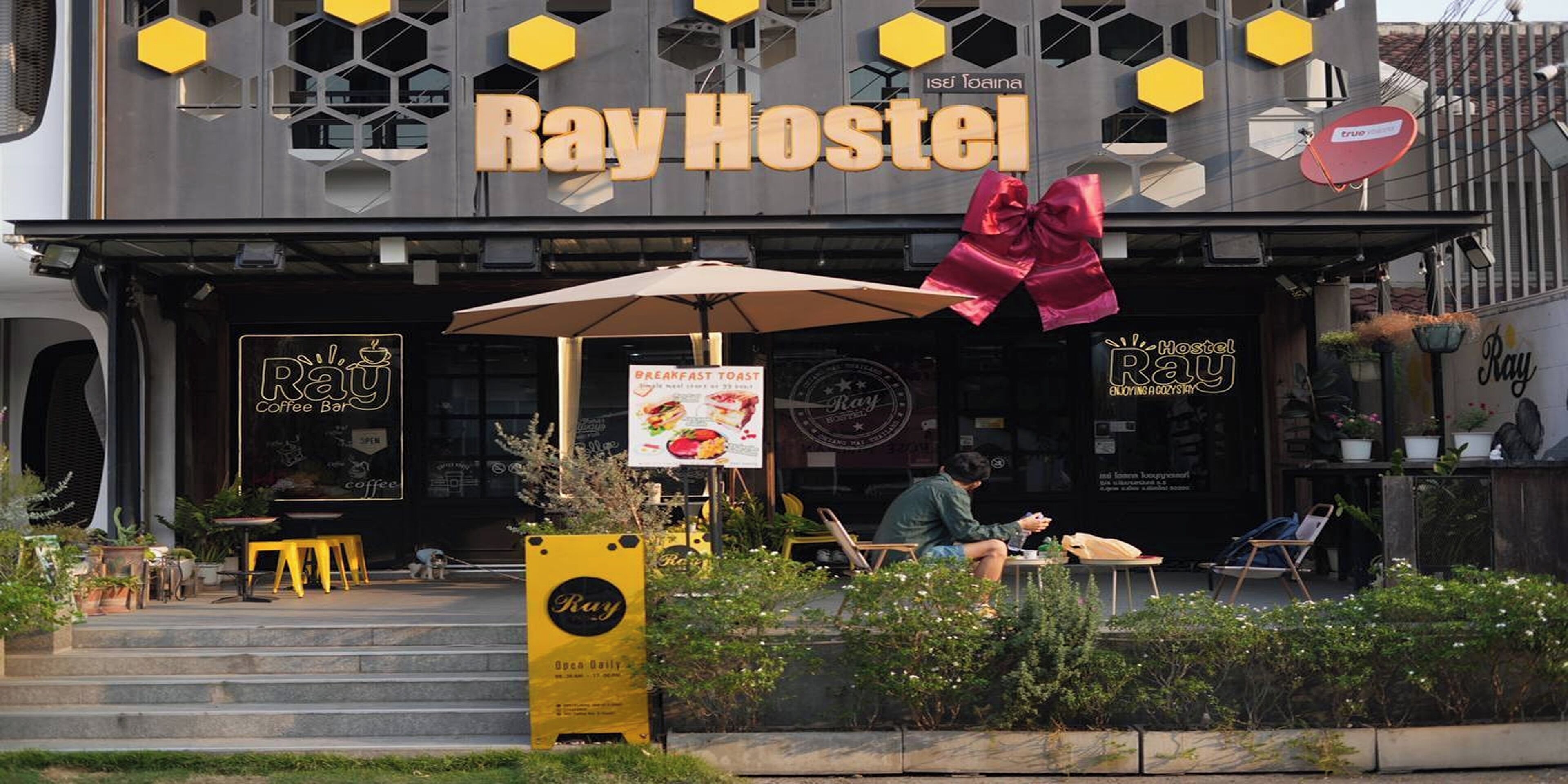 The exterior of Ray Hostel with a large sign, outdoor seating, and a yellow signboard.