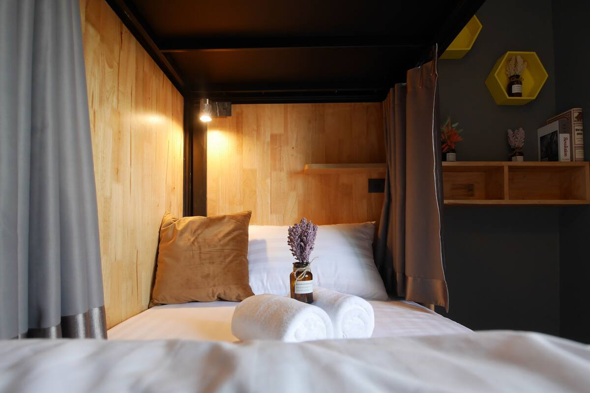 A neatly made bed with white linens, a brown pillow, and a vase with flowers.