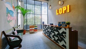 A reception area with a wooden desk, a colorful mural, a large window, and a plant. - Lopi Hotel (Makassar)