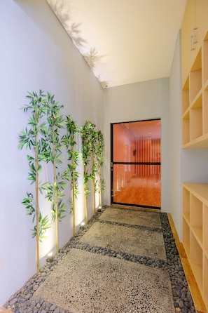 A hallway with a pebbled floor, bamboo plants, and a wooden shelf unit. - Lopi Hotel (Makassar)