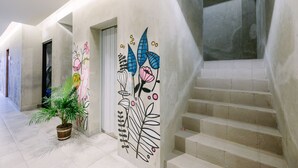 A hallway with a potted plant, a staircase, and a wall with floral artwork. - Lopi Hotel (Makassar)