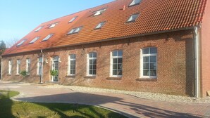 En byggnad av tegel med ett rött tegeltak, flera fönster och en plattbelagd entré.