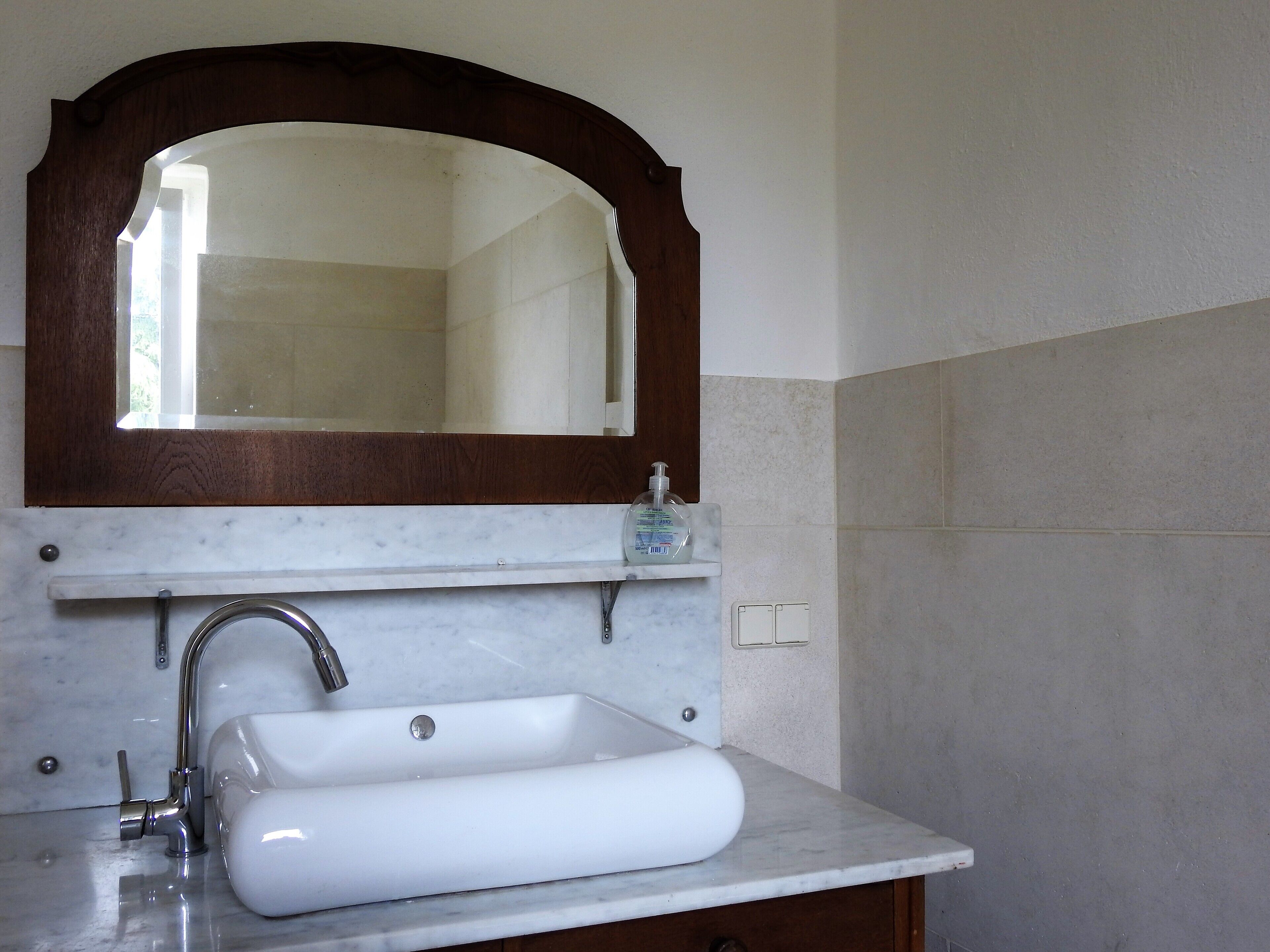 A bathroom with a white sink, a wooden-framed mirror, and a soap dispenser.