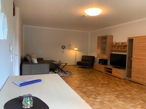 Ein modernes Wohnzimmer mit Sofa, Sessel, Fernseher, Holzschrank und einer Lampe.