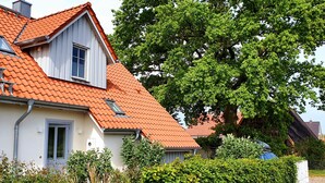 A house with a red-tiled roof, white exterior walls, and a large tree in front.