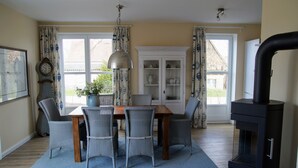 A dining room with a wooden table and six wicker chairs, a large vase with flowers, and a black stove.