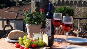 Una mesa con una botella de vino, dos copas de vino tinto, un plato de queso, un bol de uvas y una hogaza de pan.