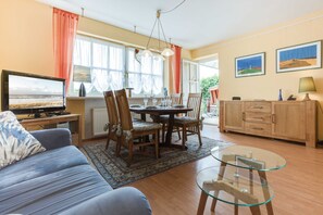 Un salon comprenant un canapé, une table basse en verre, une table à manger avec des chaises, un téléviseur et un meuble.