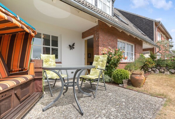 Une terrasse avec une table et des chaises, un banc en bois et une maison en briques avec un jardin.