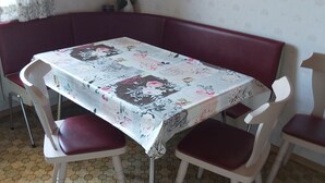 A dining area with a table covered in a floral tablecloth, surrounded by red cushioned chairs.