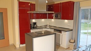 A modern kitchen with red cabinets, a central island, and a built-in microwave.