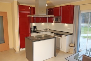 A modern kitchen with red cabinets, a central island, and a built-in microwave.