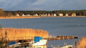 A lakeside view with boats docked near a wooden pier, surrounded by houses and a forested area.