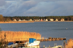 A lakeside view with boats docked near a wooden pier, surrounded by houses and a forested area.