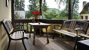 A wooden bench and table on a balcony with a view of trees and a building.