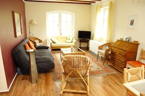 A living room with a sofa, a wicker chair, a television, a dresser, and a window with curtains.