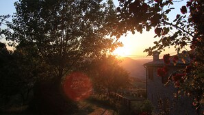 Un bâtiment rustique en pierre, avec un sentier de jardin qui y mène, entouré d’arbres et de fleurs en pleine floraison.