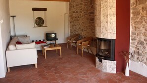 Un salon chaleureux avec une cheminée en pierre, un canapé blanc, un téléviseur et des fauteuils en osier.