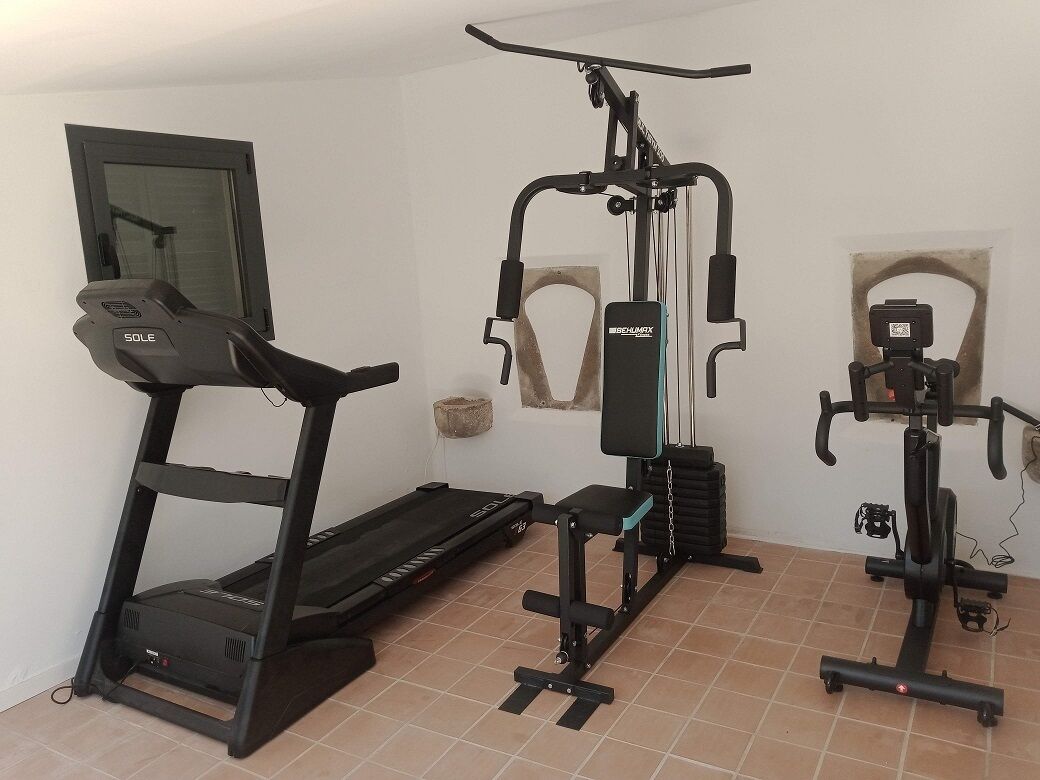 Une salle de sport à domicile équipée d’un tapis de course, d’un banc de musculation et d’un appareil elliptique.