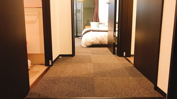 A hotel hallway with a carpeted floor leading to a bedroom with a bed and a nightstand. - GH One More Heart Enmachi 3 (Kyoto)