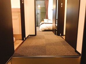 A hotel hallway with a carpeted floor leading to a bedroom with a bed and a nightstand. - GH One More Heart Enmachi 3 (Kyoto)