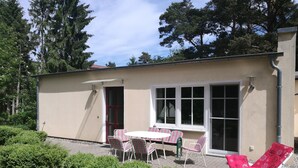 Een klein gebouw met een terras, een tafel met stoelen en twee ligbedden.