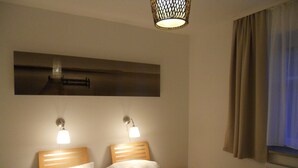 Een hotelkamer met een bed, twee bedlampen, een nachtkastje, een kunstwerk aan de muur en een raam met gordijnen.