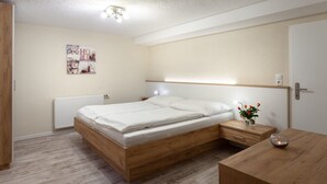 Un dormitorio con cama de madera, mesita de noche y un pequeño escritorio con un jarrón de flores.