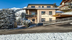 Edificio de dos pisos llamado "Haus Michael", con un paisaje nevado y montañas al fondo.