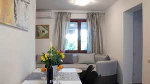 Un comedor con una mesa preparada para dos, un jarrón con flores y una ventana con cortinas.