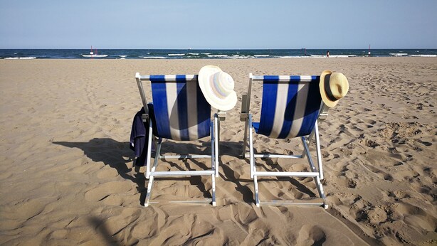 Two beach chairs with striped blue and white covers and straw hats placed on a sandy beach with a view of the ocean and a buoy in the distance. - Venetian palazzo near St. Mark's Square & Arsenal, canal view, free Wi-Fi (Venezia)