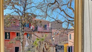 A view through a window of a building with a tree in the foreground, a brick wall, and colorful buildings in the background. - Venetian palazzo near St. Mark's Square & Arsenal, canal view, free Wi-Fi (Venezia)