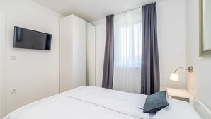 A hotel room with a bed, a TV mounted on the wall, a bedside lamp, and a window with curtains.
