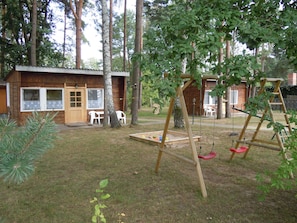 A wooden cabin with a porch, a swing set, and a play area with toys.