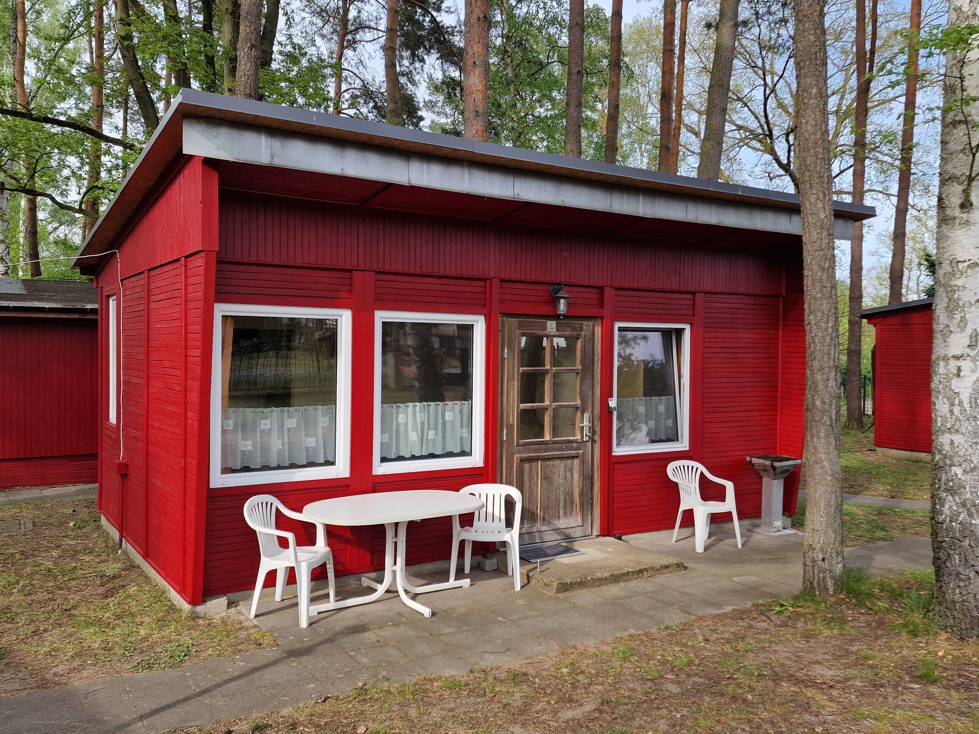 A red cabin with a small porch, two white plastic chairs, and a table.