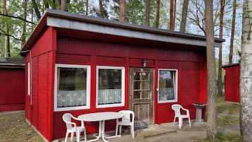 Una cabaña roja con un porche pequeño, dos sillas de plástico blancas y una mesa.