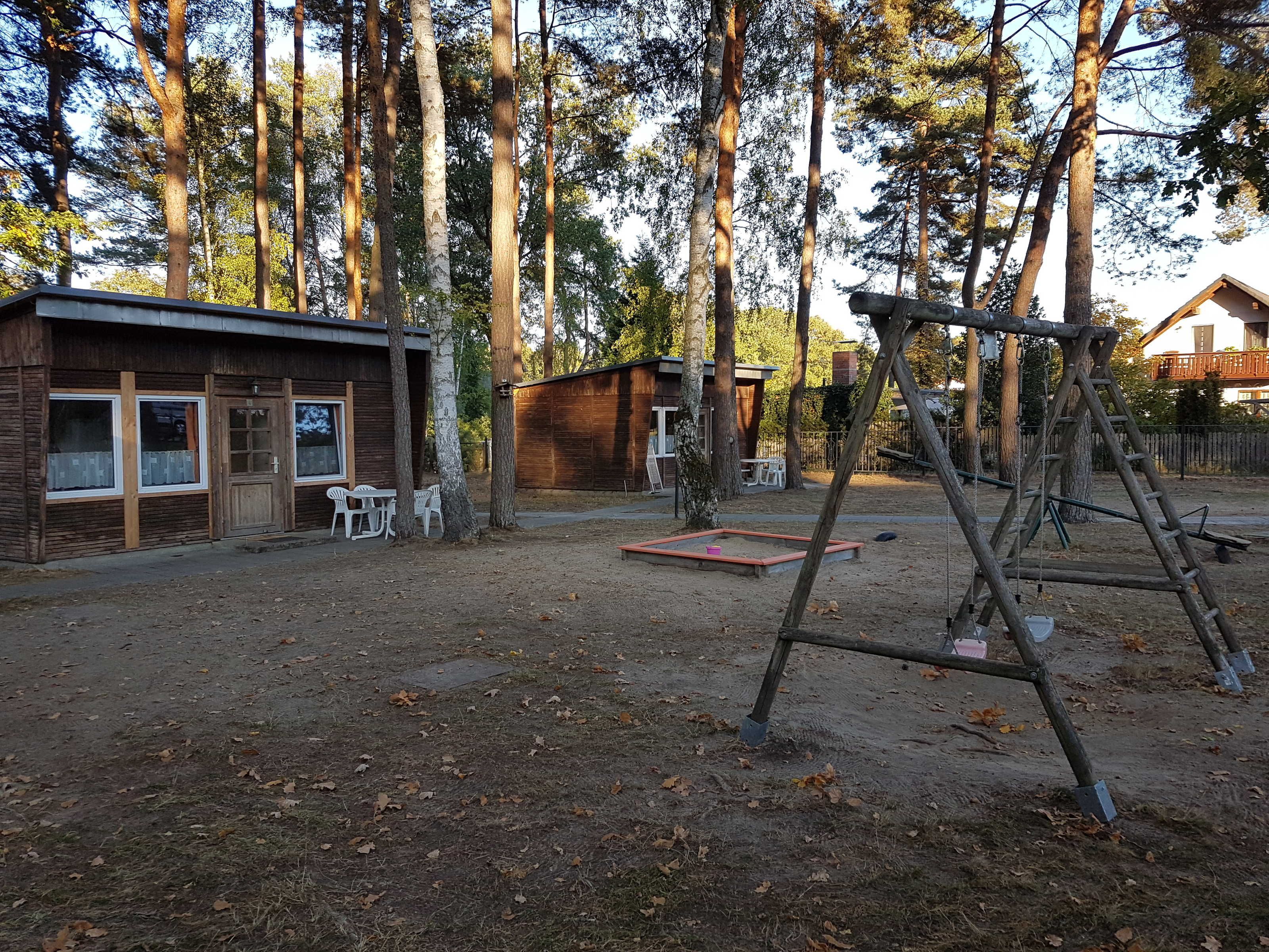 Eine rustikale Holzhütte mit einer kleinen Terrasse, Sitzgelegenheiten im Freien und einer Schaukel im Waldgebiet.