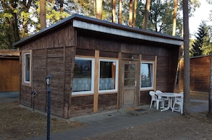 En lille træhytte med veranda, et bord med stole og et vindue med gardin.