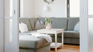 A modern living room with a grey sofa, a white coffee table, and a wooden ceiling. - Gemütl cottage + wifi, 1.5 km to the beach, fenced playground / lawn (Pommerby)