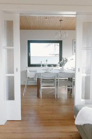 A dining area with a white table set for four, a window with a view, and a wooden ceiling.