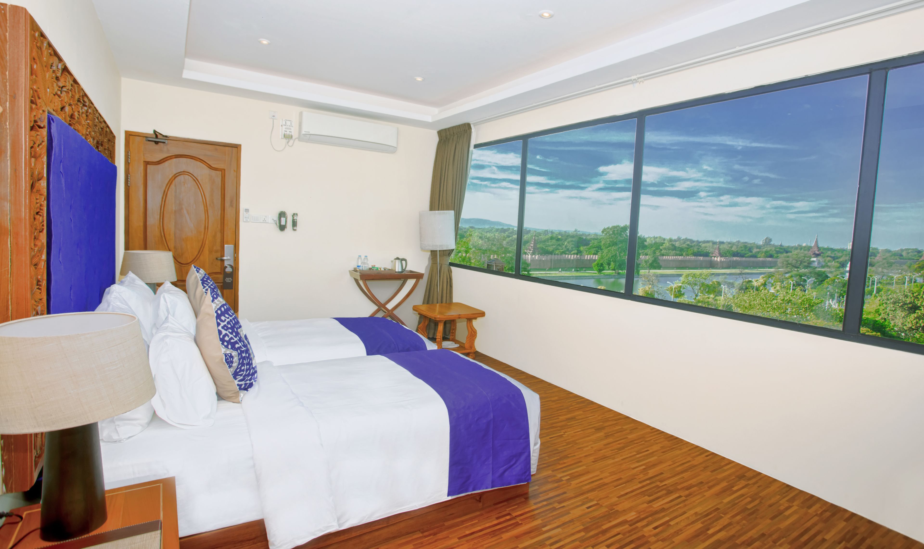 Ein Hotelzimmer mit großem Fenster und schöner Aussicht, einem ordentlich bezogenen Bett, einem kleinen Tisch mit Lampe und Holzboden.