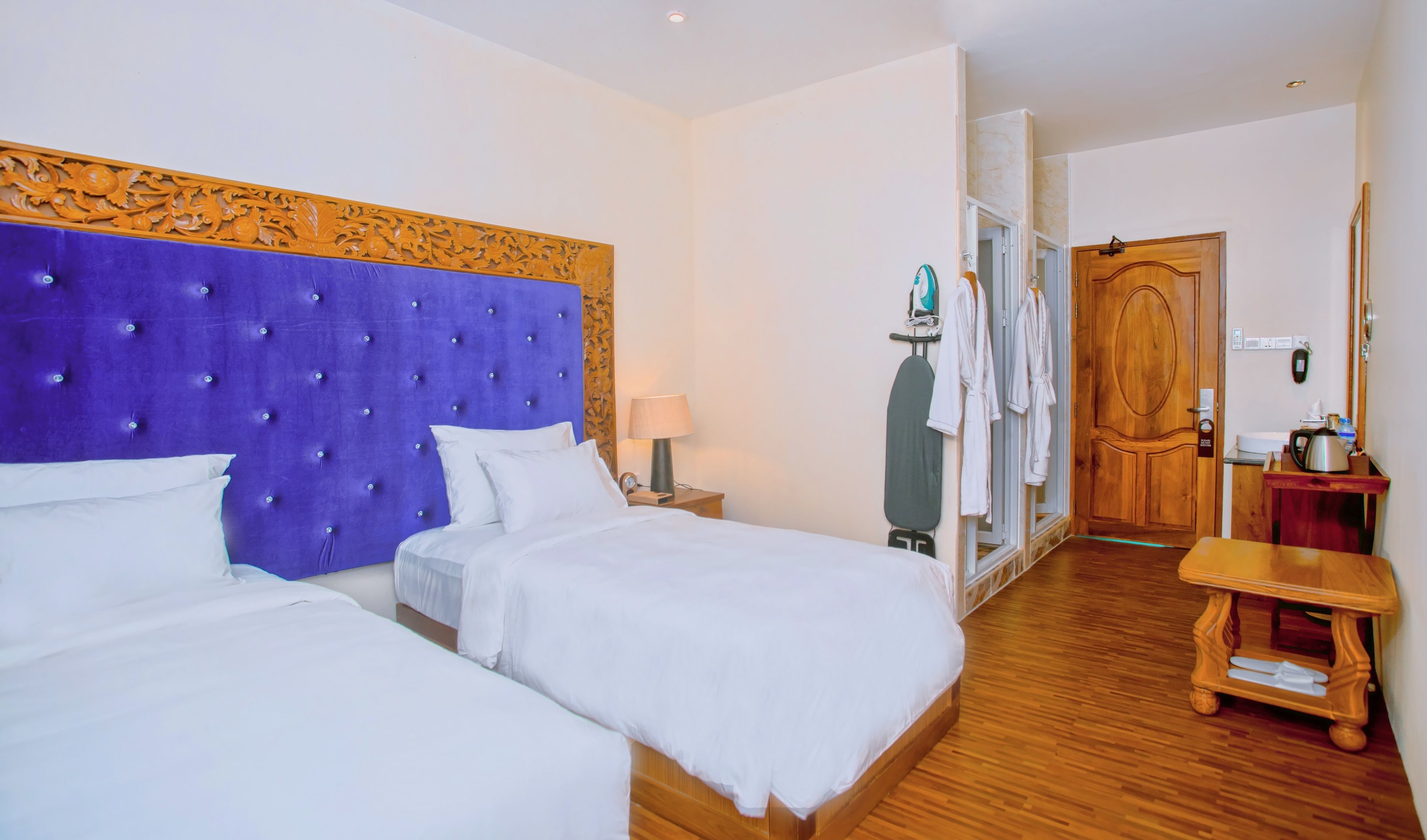 Habitación de hotel con dos camas, una puerta de madera, una mesita y un espejo.